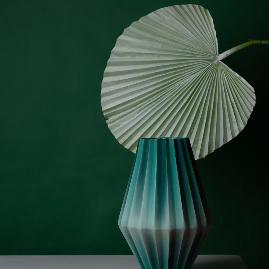 A green vase infront of a green wall