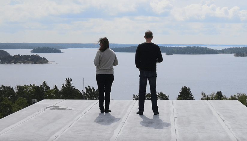 A man and a woman standing on a roof top overlooking the sea