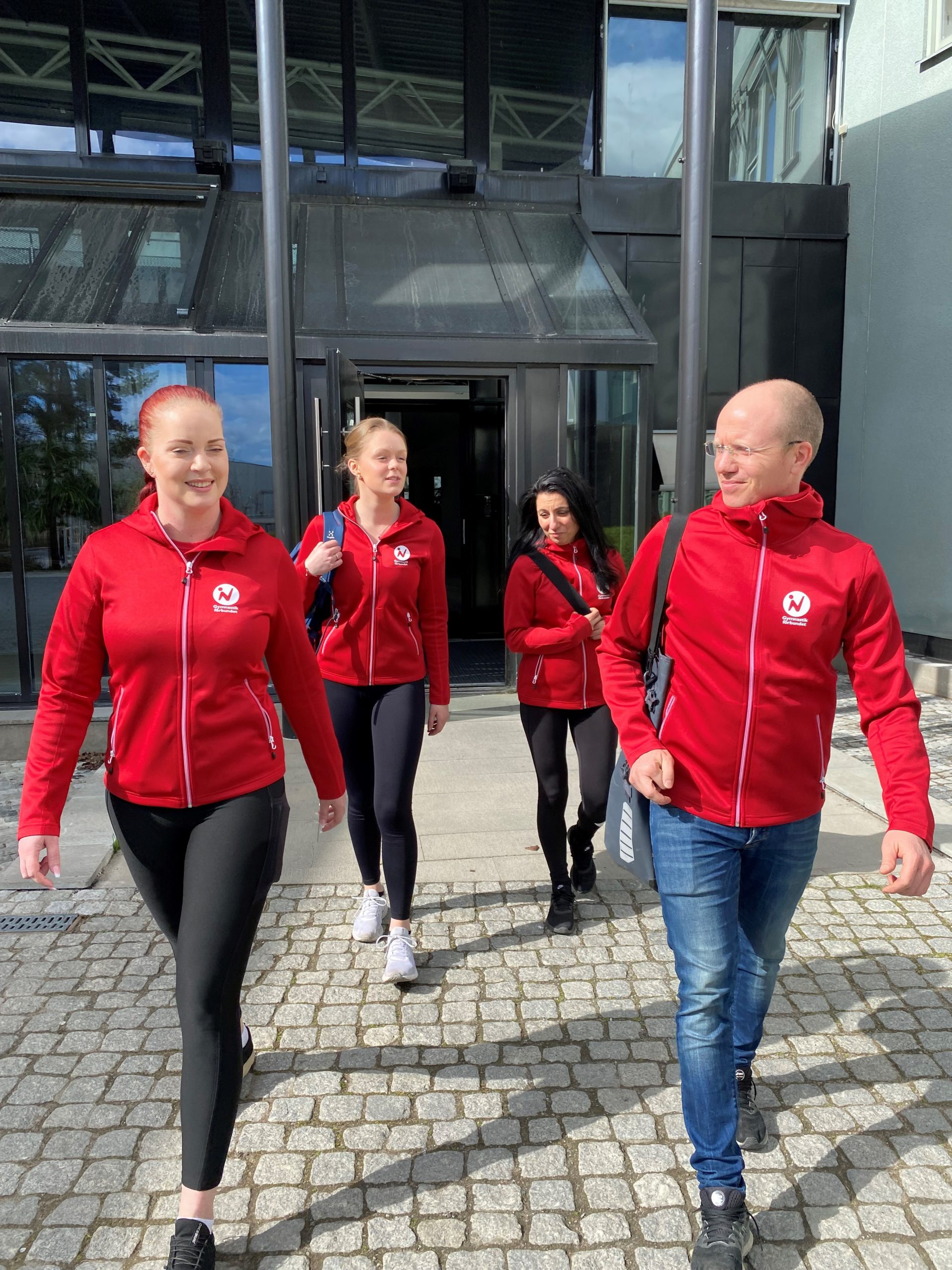 Four colleagues wearing the same red jacket walking out from a building