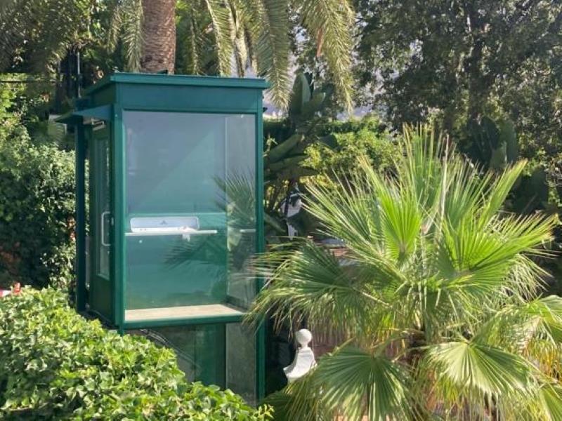 Outdoor lift in green installed in a garden. An Aritco PublicLift Access Outdoor.