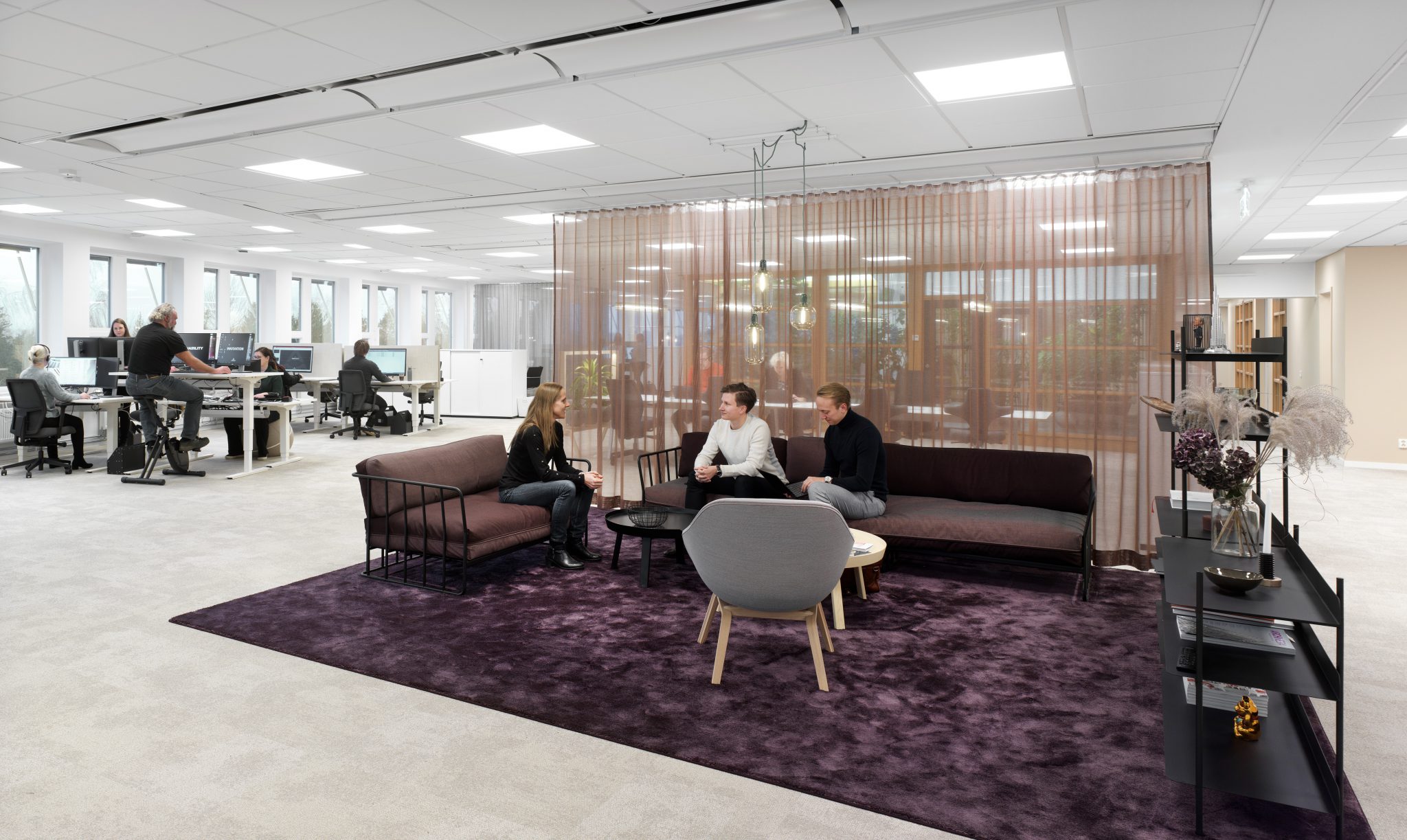 People in an office area, working by computers and sitting in a sofa chatting