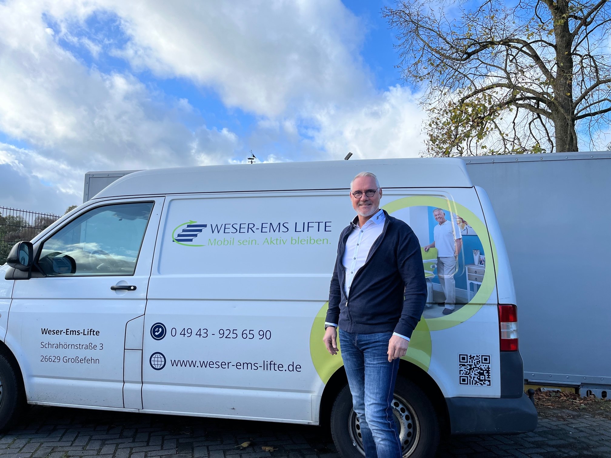 A man with white hear infront of a business car