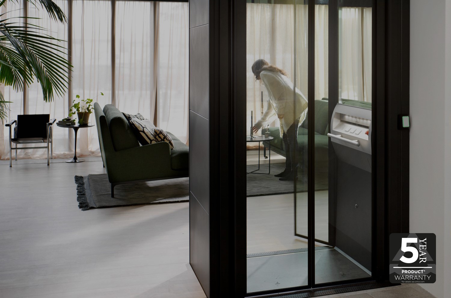 View over a livingroom with a homelift with glass walls in front